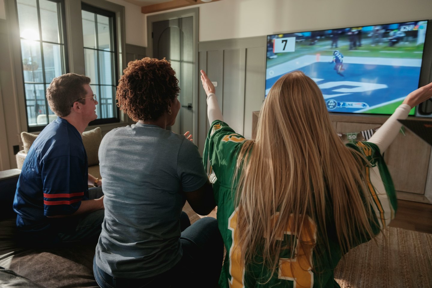 Three people watch a football game on a TV from behind.