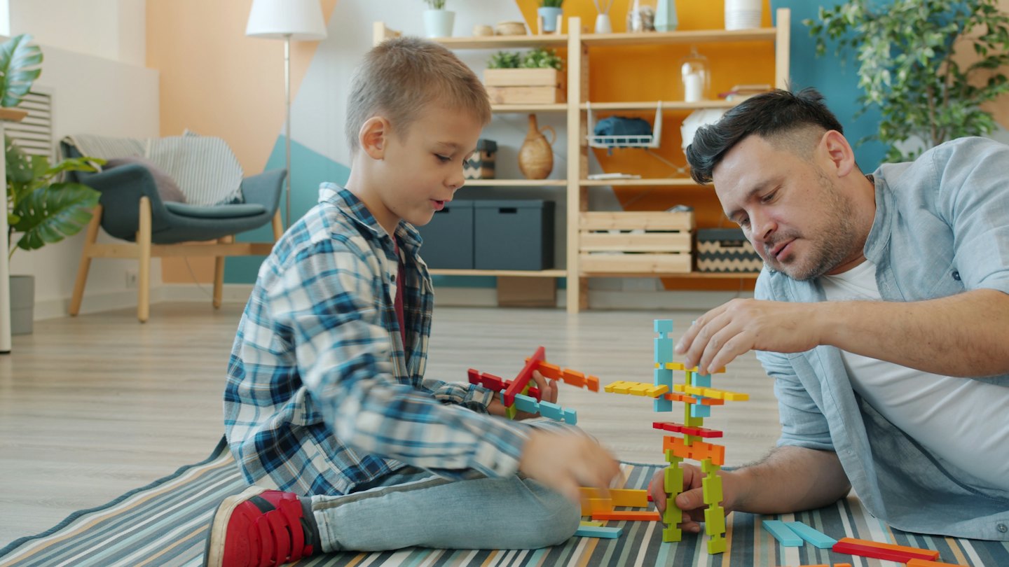 Father and son build towers with colorful blocks on a rug.