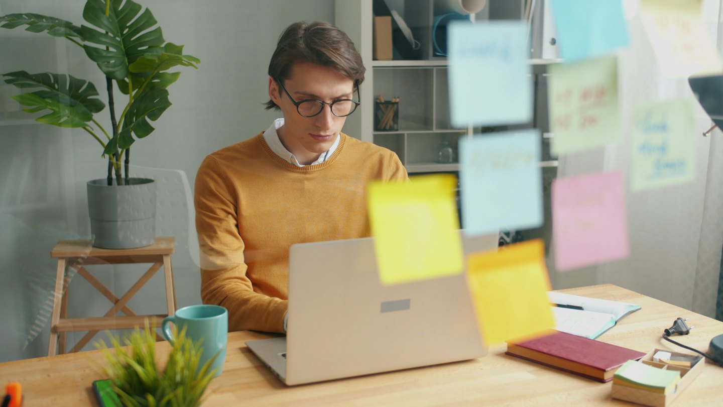 Man with glasses types on a laptop at his desk.